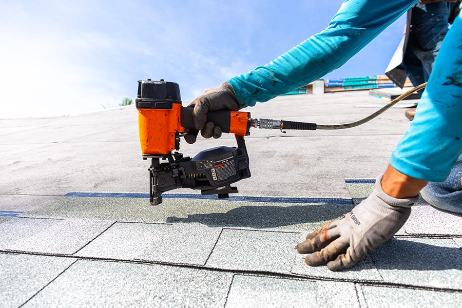 A professional roofing contractor installing shingles with a nail gun to a residential home in Central IL.