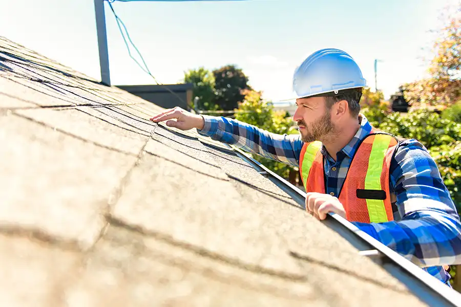 BAM Roofing & Construction—A male roofer with a vest and hard hat inspects a residential roof in Central IL.