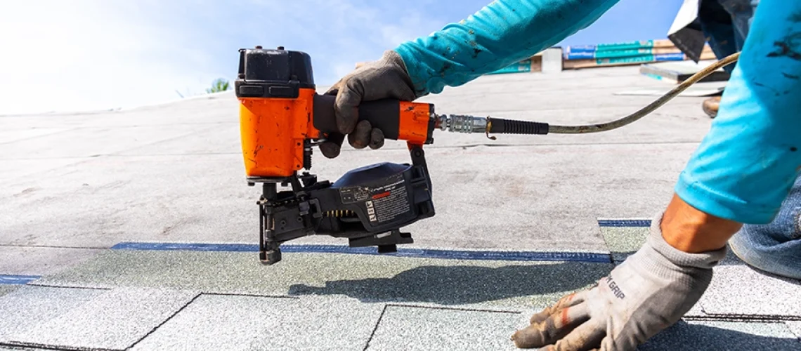 A professional roofing contractor installing shingles with a nail gun to a residential home in Central IL.